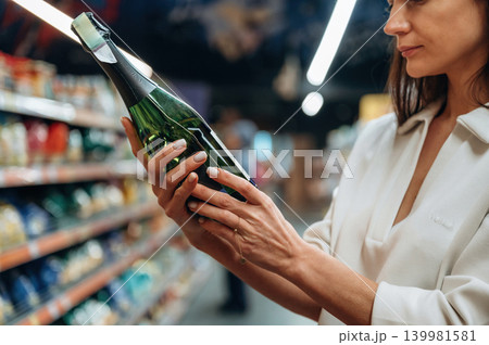 Woman examining a bottle of sparkling wine in a grocery store aisle, surrounded by colorful shelves filled with various beverages and snacks, showcasing shopping experience Woman examining a bottle of sparkling wine in a grocery store aisle, surrounded by colorful shelves filled with various beverages and snacks, showcasing shopping experience 139981581