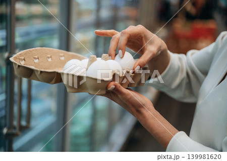 Woman selecting fresh eggs from carton in grocery store, showcasing careful choice and quality, emphasizing healthy food options and shopping experience Woman selecting fresh eggs from carton in grocery store, showcasing careful choice and quality, emphasizing healthy food options and shopping experience 139981620