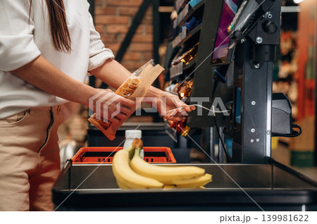 Woman shopping at self-checkout station, scanning items with focus, surrounded by colorful products and fresh produce, showcasing modern retail experience Woman shopping at self-checkout station, scanning items with focus, surrounded by colorful products and fresh produce, showcasing modern retail experience 139981622