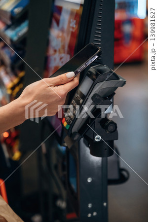 Hand holding smartphone near contactless payment terminal in a vending machine environment, showcasing modern technology and convenience in transactions Hand holding smartphone near contactless payment terminal in a vending machine environment, showcasing modern technology and convenience in transactions 139981627