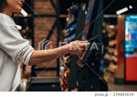 Woman using self-service kiosk to make payment in a modern retail environment, showcasing convenience and technology in shopping experience 139981639