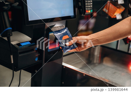 Hand of a customer using self-service checkout machine to scan a payment card, showcasing modern technology in retail environment with vibrant colors Hand of a customer using self-service checkout machine to scan a payment card, showcasing modern technology in retail environment with vibrant colors 139981644
