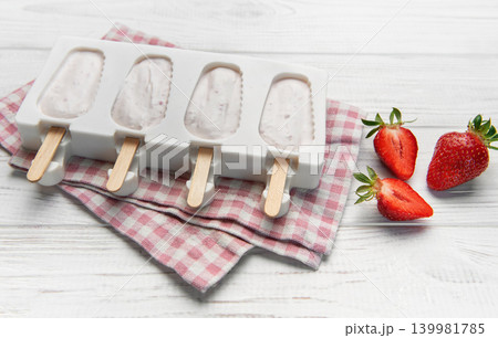 Diy strawberry yogurt popsicles chilling in mold on white wood Diy strawberry yogurt popsicles chilling in mold on white wood 139981785