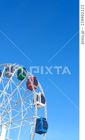 Ferris wheel cabins against blue sky in city amusement park, vertical backdrop with copy space. Children's entertainment, family weekend. Fair or market on sunny day. Symbol of Royal Easter Show Ferris wheel cabins against blue sky in city amusement park, vertical backdrop with copy space. Children's entertainment, family weekend. Fair or market on sunny day. Symbol of Royal Easter Show 139982123