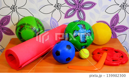 colorful sports balls and a fitness mat on a wooden table colorful sports balls and a fitness mat on a wooden table 139982300