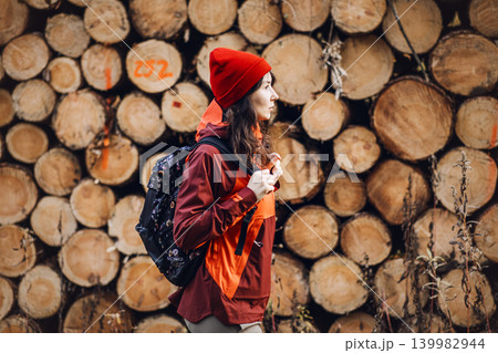 Woman walks past stacked timber logs in woodland area. Woman forest inspector, female industrial professional, environmental auditor at work. Woman walks past stacked timber logs in woodland area. Woman forest inspector, female industrial professional, environmental auditor at work. 139982944