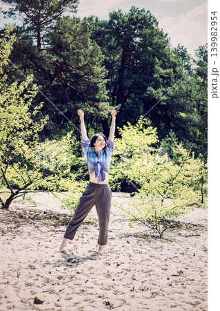 Woman stands with back to camera looking at tall trees in pine forest. Restorative forest walk, outdoor leisure activity, weekend nature getaway 139982954