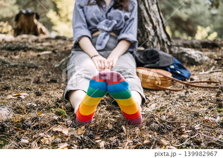Feet wearing rainbow socks rest on forest ground while person sits in background. lgbtq mental health, queer mindfulness nature, finding inner peace, mental wellness awareness. 139982967