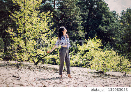 Person stands barefoot on sand in forest with outstretched arms looking up. wilderness therapy session, forest bathing experience, holistic wellness outdoor. Person stands barefoot on sand in forest with outstretched arms looking up. wilderness therapy session, forest bathing experience, holistic wellness outdoor. 139983038