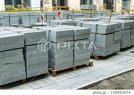Stacks of stone paving slabs sit on pallets at urban construction site. Municipal redevelopment plan, public space renovation, pedestrian zone construction. 139983074