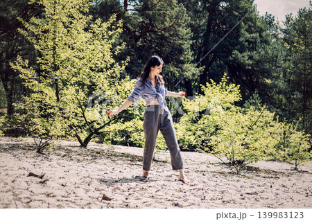 Person stands barefoot on sand in forest with outstretched arms. authentic happiness outdoors, emotional release exercise, catching sun, inner peace journey. Person stands barefoot on sand in forest with outstretched arms. authentic happiness outdoors, emotional release exercise, catching sun, inner peace journey. 139983123