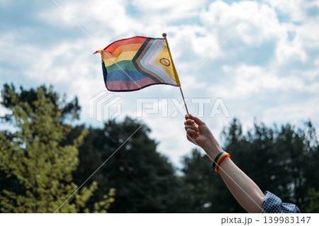 Hand holds inclusive pride flag toward sky. LGBTQ Identity, gender expression, authentic self, pride symbol. Hand holds inclusive pride flag toward sky. LGBTQ Identity, gender expression, authentic self, pride symbol. 139983147