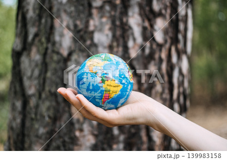 Hand holds small globe against blurred tree trunk background. Green corporate strategy, environmental social governance, sustainable development goals. 139983158