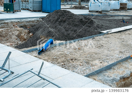 Construction site shows excavated ground with soil mounds and protruding pipes next to stone pavement. Urban redevelopment, infrastructure improvement, city planning. Construction site shows excavated ground with soil mounds and protruding pipes next to stone pavement. Urban redevelopment, infrastructure improvement, city planning. 139983176