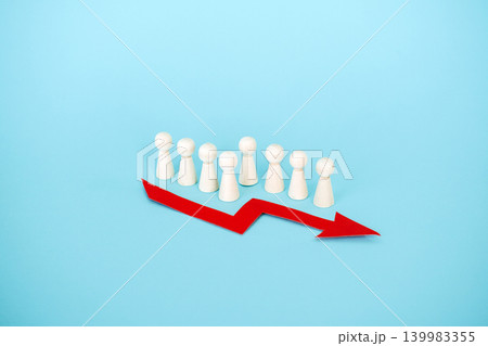 Line of wooden peg dolls stands behind red downward arrow on blue background. Corporate mass layoffs, rising unemployment rate, job market instability, Human resources crisis. Line of wooden peg dolls stands behind red downward arrow on blue background. Corporate mass layoffs, rising unemployment rate, job market instability, Human resources crisis. 139983355