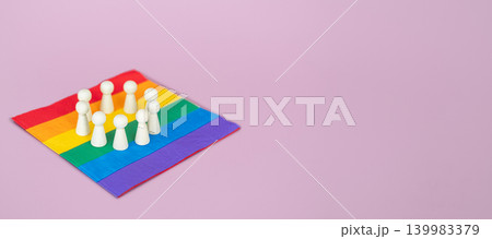 Group of wooden figurines stands in circle on rainbow pride flag against pink background. DEI Diversity, Equity, and Inclusion policy implementation, inclusive corporate culture, workplace equity. 139983379