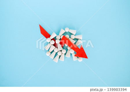 Red downward arrow lies on pile of wooden peg dolls over blue background. Mass layoffs 2026, workforce reduction impact, global unemployment surge, Economic recession. 139983394