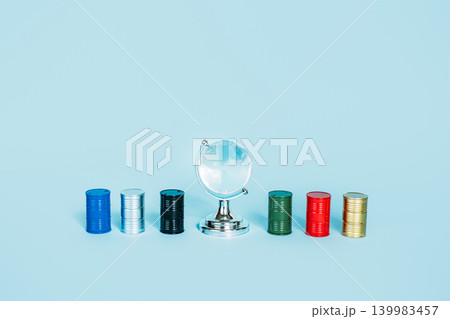 Glass globe sits surrounded by colorful miniature oil barrels on light blue background. Global oil dependency, fossil fuel foundation, energy-driven world economy. Glass globe sits surrounded by colorful miniature oil barrels on light blue background. Global oil dependency, fossil fuel foundation, energy-driven world economy. 139983457