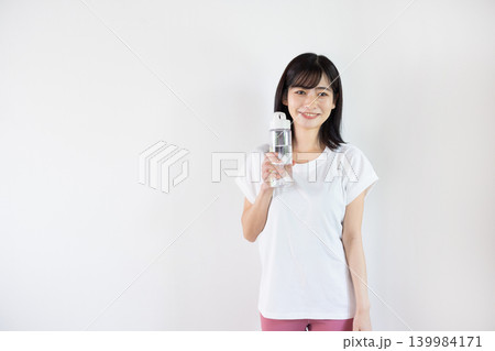 白い背景の前でウォーターボトルを手に微笑む日本人の若い女性 白い背景の前でウォーターボトルを手に微笑む日本人の若い女性 139984171