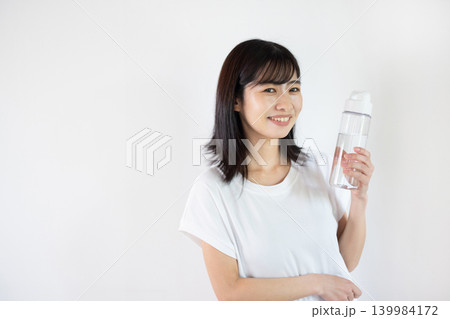 白い背景の前でウォーターボトルを手に微笑む日本人の若い女性 139984172