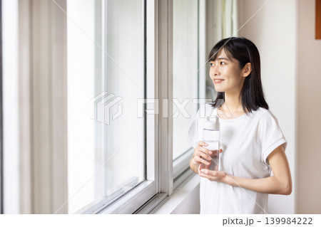 窓際でウォーターボトルを手に微笑む日本人の若い女性 139984222