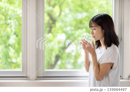 水の入ったグラスを手に窓の外を眺める日本人の若い女性 水の入ったグラスを手に窓の外を眺める日本人の若い女性 139984497