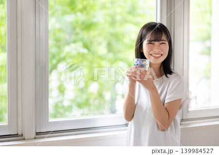 窓際で水の入ったグラスを手にカメラ目線で微笑む日本人の若い女性 窓際で水の入ったグラスを手にカメラ目線で微笑む日本人の若い女性 139984527