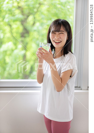 窓際で水の入ったグラスを手にカメラ目線で微笑む日本人の若い女性 窓際で水の入ったグラスを手にカメラ目線で微笑む日本人の若い女性 139984528