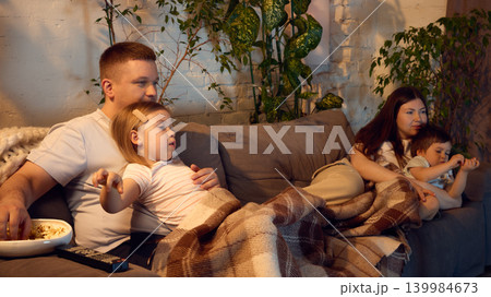 Cozy family relaxing under blanket while watching movie together in living room. 139984673