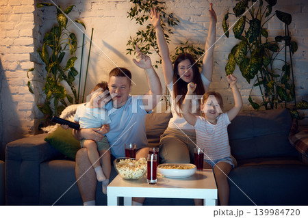 Family cheering during home movie night with popcorn and juice. Family cheering during home movie night with popcorn and juice. 139984720