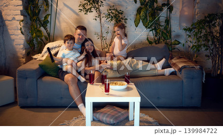 Parents and children relaxing on sofa during quiet movie evening. Parents and children relaxing on sofa during quiet movie evening. 139984722