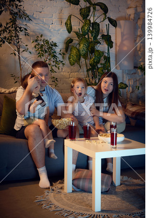 Family watching suspenseful movie on sofa with popcorn and berry drinks. 139984726