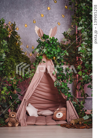 Cozy children's teepee tent in a fairytale forest interior with toys and fairy lights Cozy children's teepee tent in a fairytale forest interior with toys and fairy lights 139985208