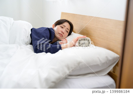 寝不足で目覚まし時計を止める日本人女性 寝不足で目覚まし時計を止める日本人女性 139986184