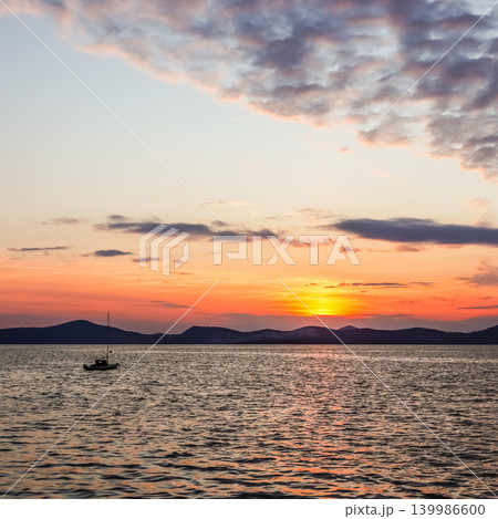 Calm evening sunset with a sailboat on the water, reflecting vibrant colors across the sky in Gulluk, Turkey Calm evening sunset with a sailboat on the water, reflecting vibrant colors across the sky in Gulluk, Turkey 139986600