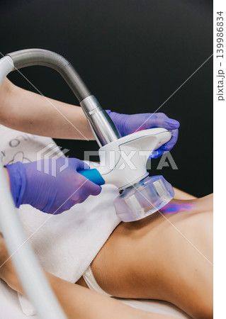 Close-up of a young woman receiving professional body contouring massage treatment for slimming and cellulite reduction in a beauty clinic. Non-invasive aesthetic procedure, skincare, body care Close-up of a young woman receiving professional body contouring massage treatment for slimming and cellulite reduction in a beauty clinic. Non-invasive aesthetic procedure, skincare, body care 139986834