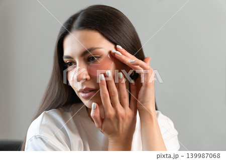 Young woman relaxing with hydrogel under-eye patches during daily skincare routine at home. Natural beauty portrait focused on self-care, healthy skin and modern cosmetic treatment. Young woman relaxing with hydrogel under-eye patches during daily skincare routine at home. Natural beauty portrait focused on self-care, healthy skin and modern cosmetic treatment. 139987068