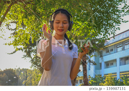 Happy young Asian women using phone and wearing headphone listen to music during exercise outdoor. Happy young Asian women using phone and wearing headphone listen to music during exercise outdoor. 139987131