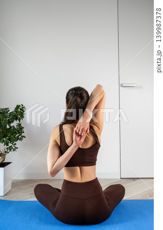 Vertical portrait of a fit young woman performing stretching and fitness exercises with resistance band at home. Female training indoors in sportswear during wellness and healthy lifestyle routine Vertical portrait of a fit young woman performing stretching and fitness exercises with resistance band at home. Female training indoors in sportswear during wellness and healthy lifestyle routine 139987378