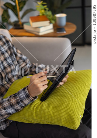 Person sitting on sofa holding digital tablet and drawing at home. Person sitting on sofa holding digital tablet and drawing at home. 139987395