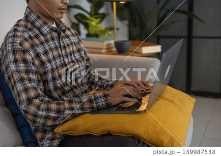 Close-up man in casual cloth sitting on sofa at home using computer for remote work or online studying Close-up man in casual cloth sitting on sofa at home using computer for remote work or online studying 139987538