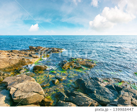 sea coast with stones and boulders in the forenoon. view of beach with rock in seaweed. dynamic cloudscape on the sky over horizon. summer vacations background concept. seaside of bulgaria, europe sea coast with stones and boulders in the forenoon. view of beach with rock in seaweed. dynamic cloudscape on the sky over horizon. summer vacations background concept. seaside of bulgaria, europe 139988447
