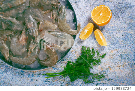 Fresh raw shrimp spread on ice with lemon and cilantro slices on a marble surface, ready to cook, no people Fresh raw shrimp spread on ice with lemon and cilantro slices on a marble surface, ready to cook, no people 139988724