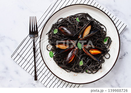 Black spaghetti with mussels, on a white plate with a fork, on a striped napkin,marble background, homemade, no people 139988726