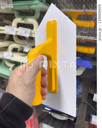 Bright yellow trowel held by hand in a hardware store aisle Bright yellow trowel held by hand in a hardware store aisle 139989409