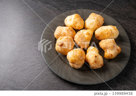 Cheese bread, a delicious Brazilian cheese bread, on a black plate on a dark surface, selective focus. Cheese bread, a delicious Brazilian cheese bread, on a black plate on a dark surface, selective focus. 139989438