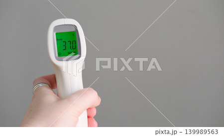 Hand holding infrared thermometer for temperature measure showing subfebrile 37 celsius degrees on green screen. Remote measurement of fever for children and public places, copy space. Flu season Hand holding infrared thermometer for temperature measure showing subfebrile 37 celsius degrees on green screen. Remote measurement of fever for children and public places, copy space. Flu season 139989563