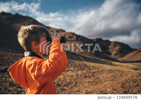 Portrait of boy tourist looking in binoculars in mountains Portrait of boy tourist looking in binoculars in mountains 139989576