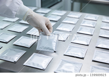 Gloved hand arranging sealed foil packets on a sterile laboratory surface Gloved hand arranging sealed foil packets on a sterile laboratory surface 139989923