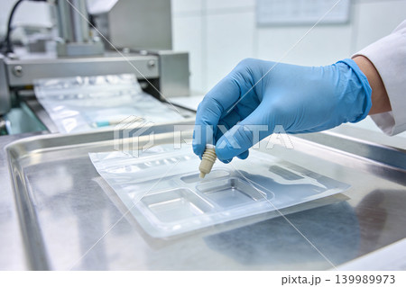 Scientist in blue gloves carefully places a small vial into a sterile medical packaging tray 139989973